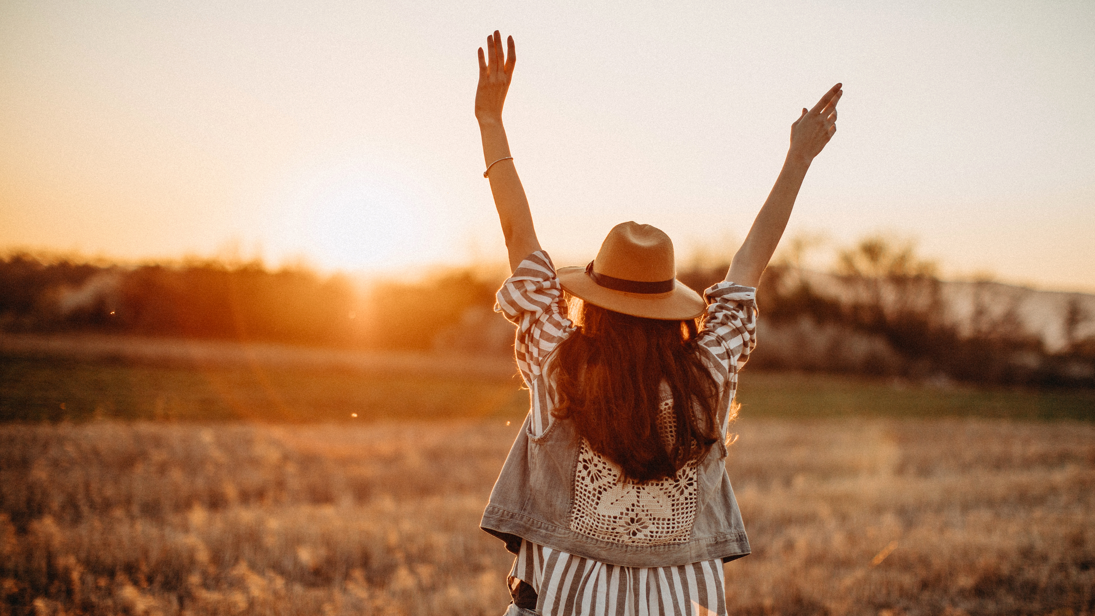 Woman with arms raised in a field at sunset